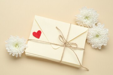 Stack of love letters, flowers and red heart on beige background, flat lay
