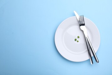Plate with fresh green peas and cutlery on light blue background, top view. Space for text