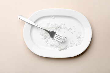 Dirty plate with rice and fork on beige background, top view