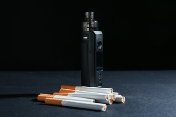 Electronic smoking device and cigarettes on dark table against black background, closeup