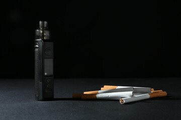 Electronic smoking device and cigarettes on dark table against black background, closeup