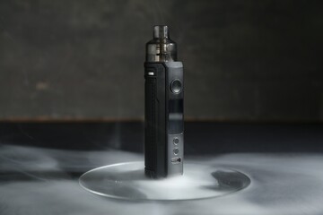 One electronic smoking device in smoke on dark table against grey background, closeup