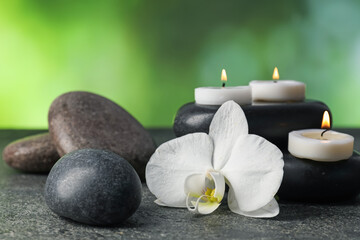 Spa stones, burning candles and orchid flower on grey table, closeup