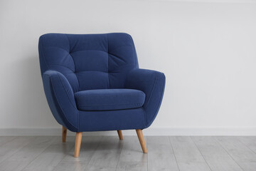 Comfortable blue armchair near white wall indoors, space for text