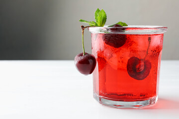 Tasty cherry soda with ice cubes, mint and berries on white wooden table, closeup. Space for text