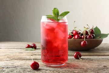 Tasty cherry soda with ice cubes, berries and mint on wooden table, closeup