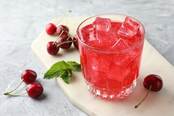 Tasty cherry soda with ice cubes, berries and mint in glass on grey textured table, closeup