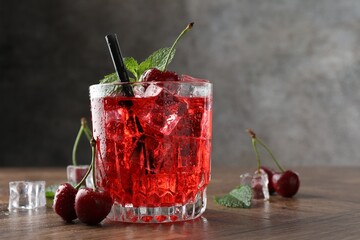 Tasty cherry soda with ice cubes, berries and mint in glass on wooden table, closeup. Space for text