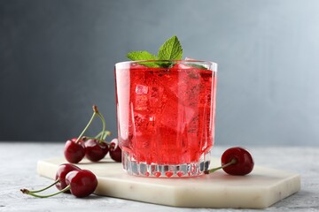 Tasty cherry soda with ice cubes, berries and mint in glass on grey textured table, closeup