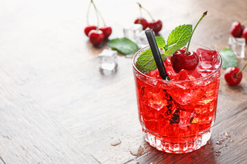 Tasty cherry soda with ice cubes, berries and mint in glass on wooden table, closeup. Space for text