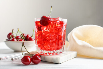 Tasty cherry soda with ice cubes and berries in glass on white wooden table, closeup