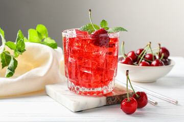 Tasty cherry soda with ice cubes, berries and mint in glass on white wooden table, closeup