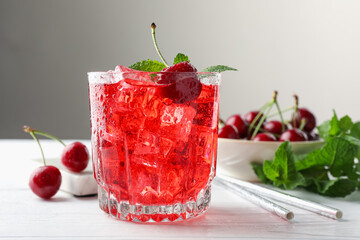 Tasty cherry soda with ice cubes, berries and mint in glass on white wooden table, closeup