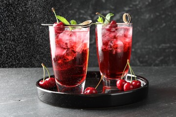 Tasty cherry soda with ice cubes, berries and mint in glasses on grey table, closeup