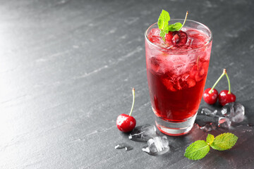 Tasty cherry soda with ice cubes, berries and mint in glass on grey table, closeup. Space for text