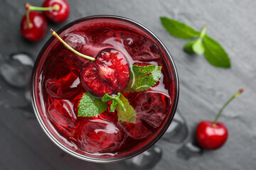 Tasty cherry soda with ice cubes, berries and mint in glass on grey table, flat lay
