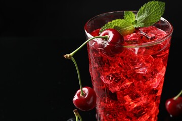 Tasty cherry soda with ice cubes, berries and mint in glass on black background, closeup. Space for text