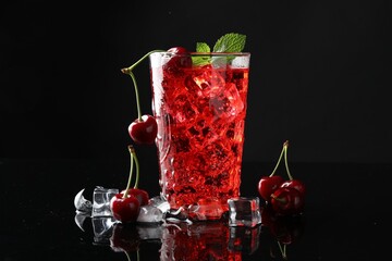 Tasty cherry soda with ice cubes, berries and mint in glass on black background, closeup
