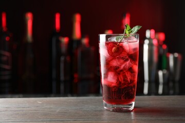 Tasty cherry soda water with ice cubes, berry and mint in glass on wooden table against blurred background, space for text