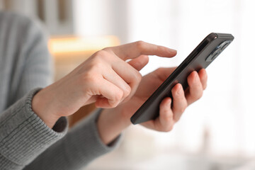 Woman using modern smartphone at home, closeup