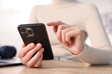 Woman using modern smartphone at wooden table indoors, closeup