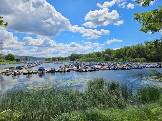 Large body of water with many boats docked. The water is blue and the sky is cloudy in backwater river