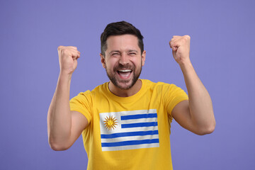 Happy fan with flag of Uruguay on his t-shirt against dark violet background
