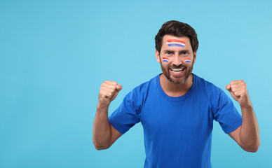 Excited fan with flags of Netherlands painted on his face against light blue background. Banner...