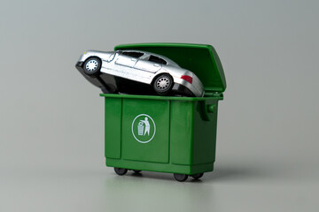 A toy car inserted into a green trash bin. Vehicle disposal, car write-offs, old car issues,...