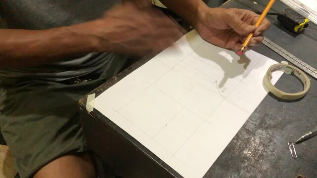 man is drafting a house plan using a pencil and T-square on a piece of bond paper at his desk.