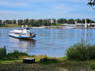 Boat is traveling on a river Volga in Yaroslavl. The boat is blue and white. There are several...