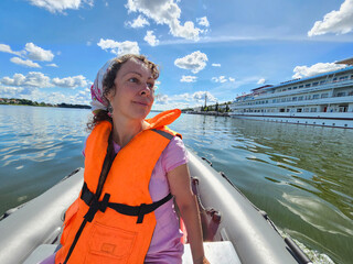 Woman wearing an orange life jacket is sitting in a motor inflatable boat on a lake. The boat is...