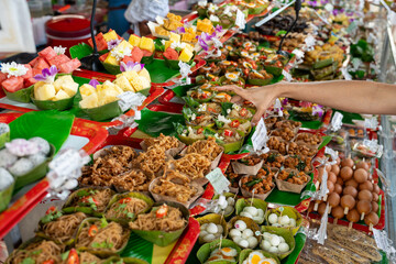 Hand of woman are picking up various foods in a basket made from banana leaves t a market in...