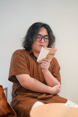 A young Chinese man in his early twenties, wearing glasses, sits in a stylish cafe, deeply focused...