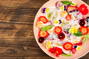 Fruit salad decorated with flowers on wooden surface.