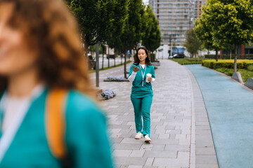 Healthcare workers in green scrubs walk on an urban path in the morning, balancing coffee and...