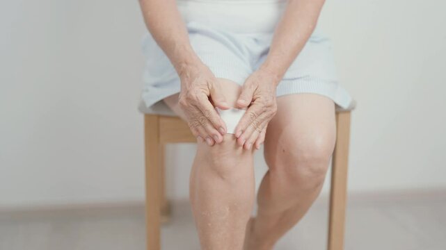 Elderly woman having knee ache with Medicated pain relief patch plaster to Runners Knee or Patellofemoral Pain Syndrome, osteoarthritis, arthritis, rheumatism and Patellar Tendinitis. Senior health