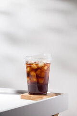 Iced Americano with ice cubes in a plastic cup on a wooden coaster. Minimalist style, perfect for...