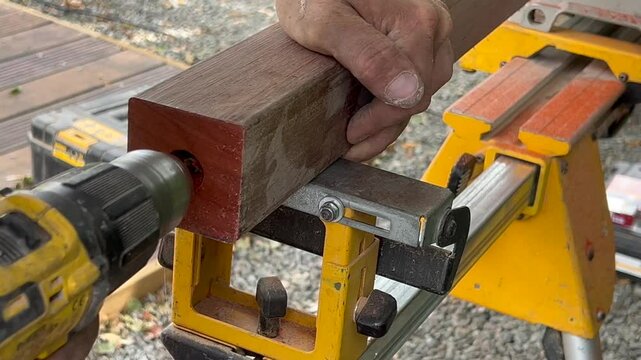 The drill makes a hole in the padouk wood poles for the construction of the hedge, building material.High quality 4k footage