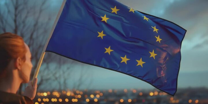 Junge Frau vor Skyline einer Stadt h&auml;lt Europafahne in der Hand