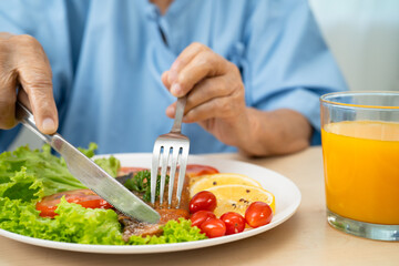 Asian elderly woman patient eating salmon stake and vegetable salad for healthy food in hospital.