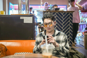Two young Chinese men in their early twenties, both wearing glasses, are drinking beverages, using...