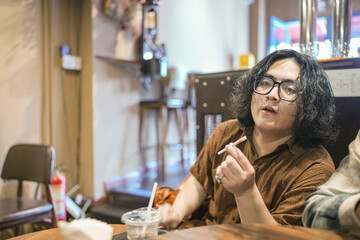 Two young Chinese men in their early twenties, both wearing glasses, are drinking beverages, using...