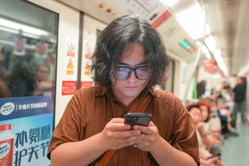 A young Chinese man in his early twenties, wearing glasses and a dark jacket, is sitting inside a...