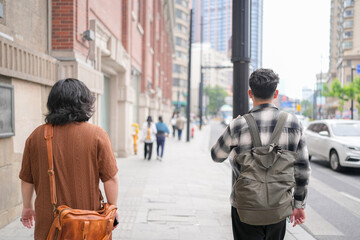 Two young Chinese men in their early twenties, both wearing glasses, walk side by side along the...