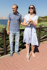 Blind woman holding white cane standing near man in park