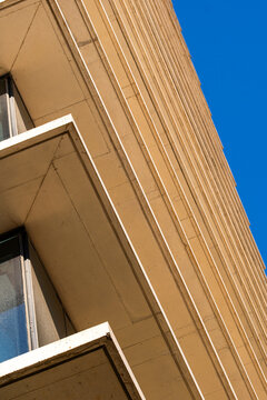 Minimalist facade detail in soft beige tones illuminated by warm sunlight, showing vertical geometric panels and clean surfaces for contemporary urban architectural design.