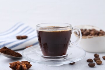Cup of aromatic coffee, beans and star anise on white table, closeup
