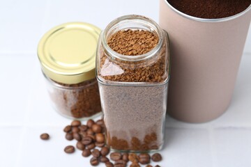 Instant coffee in jars and beans on white tiled table, closeup