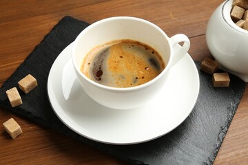 Tasty coffee in cup and sugar cubes on wooden table, closeup